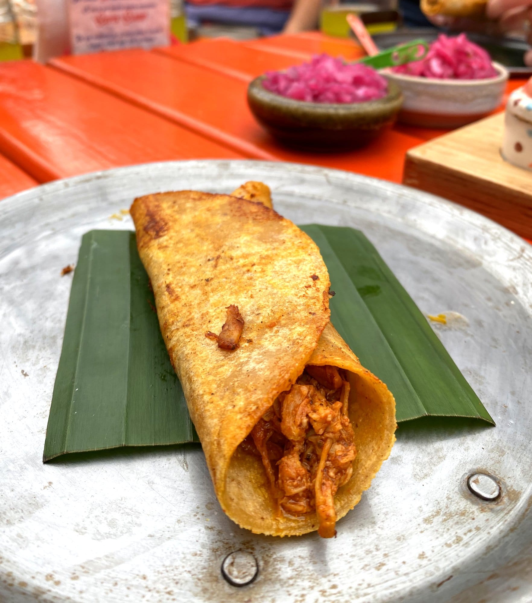 Crispy barbacoa taco on a metal plate with colorful pickled red onions at a Mexico City food tour stop
