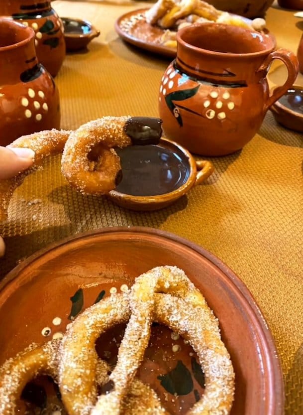 Hand dipping a sugar-dusted churro into Mexican chocolate in a clay dish at a churro-making class in Mexico City