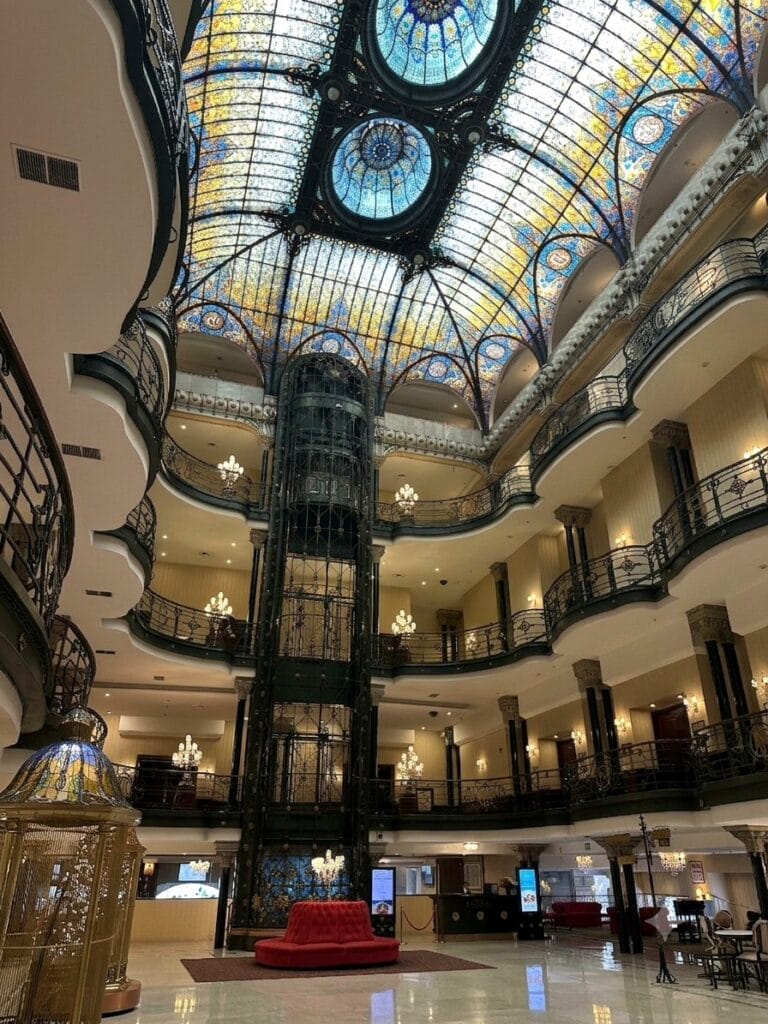 The Art Nouveau stained-glass ceiling and original caged elevator in the lobby of the Gran Hotel Ciudad de México