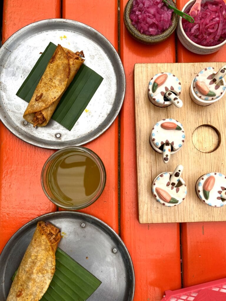A spread of tacos on tin plates with salsas and a green agua fresca on a Mexico City taco bike tour