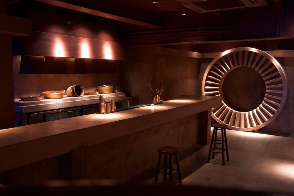 Dimly lit concrete interior of Tlecan mezcal bar with a circular sun sculpture in Roma Norte, Mexico City