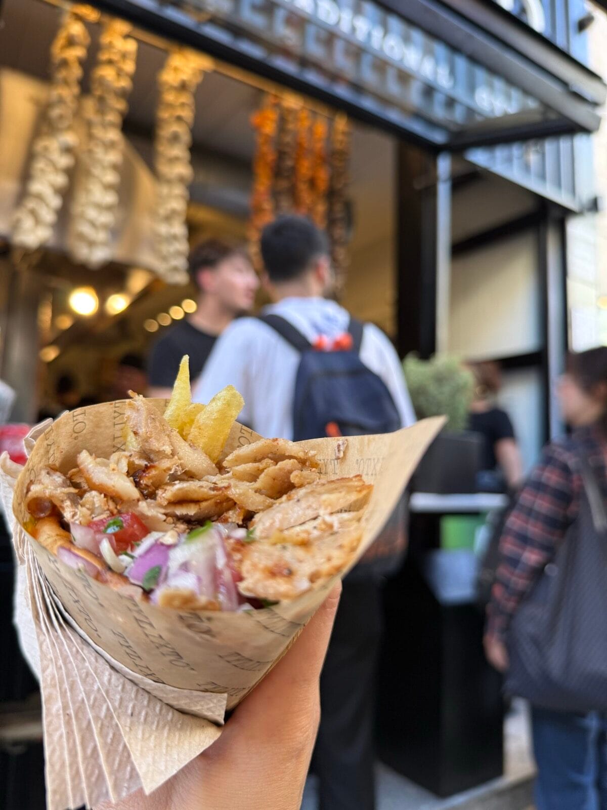 A loaded Greek gyro wrap held in front of the rotisserie at Tylixto in Athens
